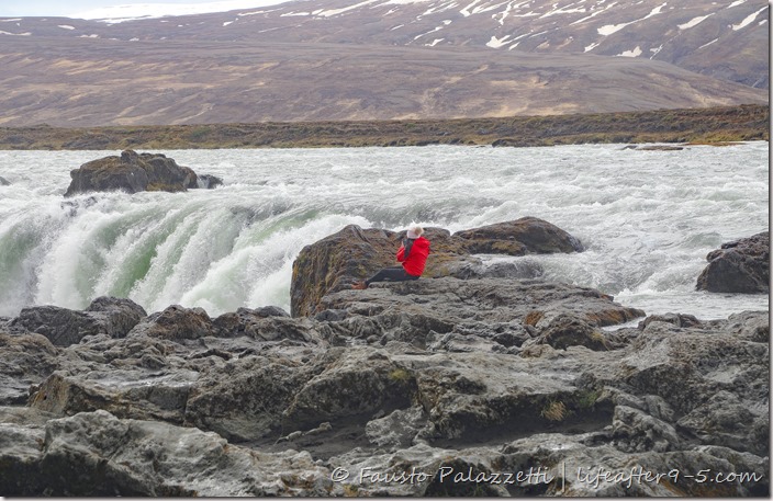 Women in red jacket sitting at the edge of Góðafoss 