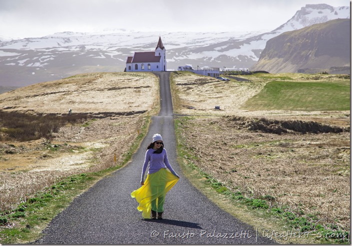 Woman on empty street in Ingjaldshóll with church and mountain background